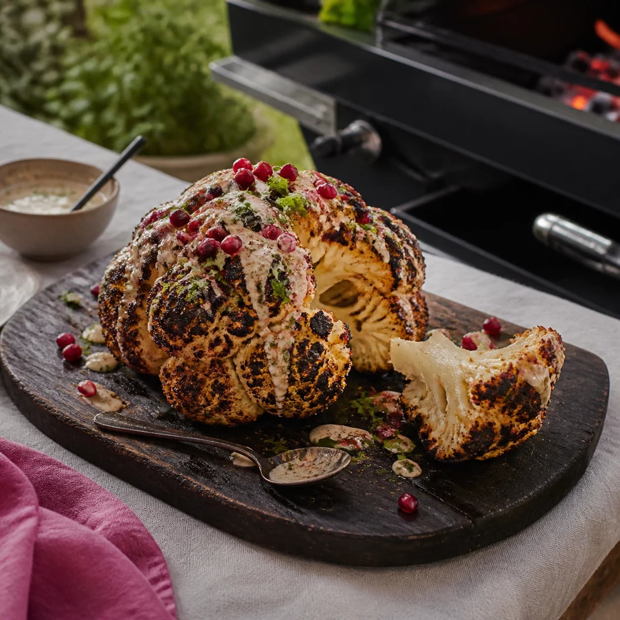 Whole barbequed cauliflower with tahini and pomegranate on a serving board