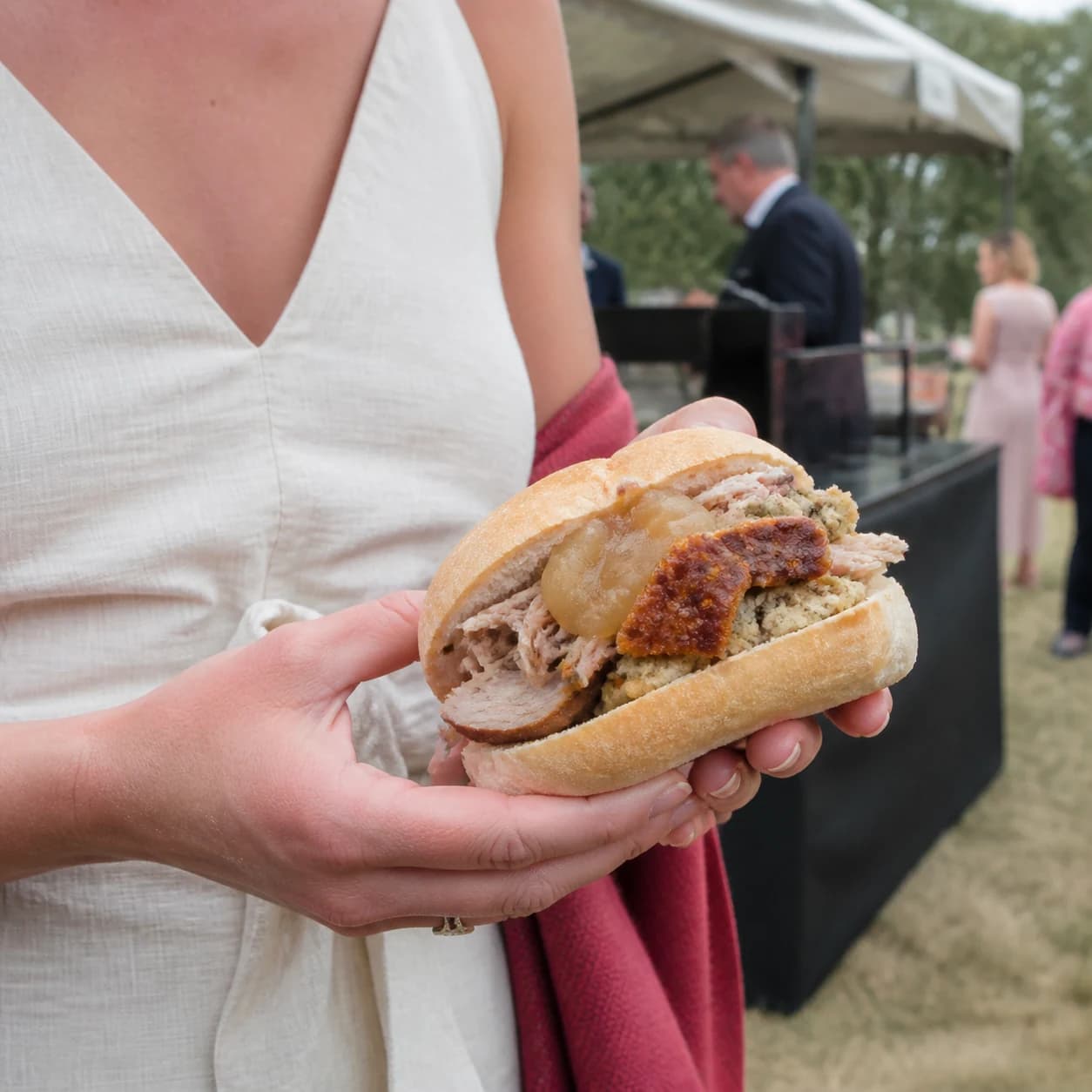 Hog roast bap with apple sauce and stuffing held in both hands